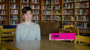 Boy named Tommy in school library speaking into a camera for an interview.