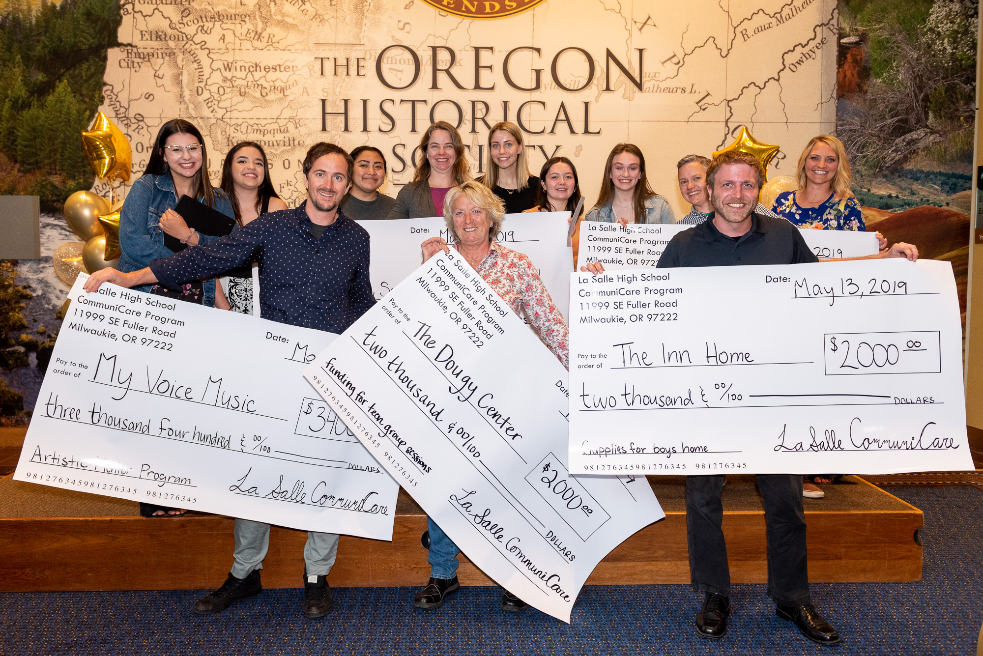 A group of students and nonprofit grant recipients holding large checks on stage at the CommuniCare Grant Awards Ceremony.