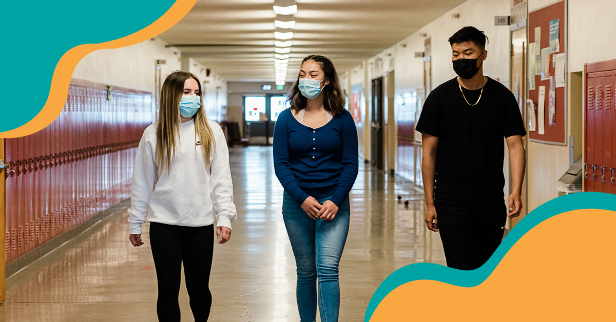 Three students wearing masks walking down a school hallway.