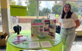 Student standing next to table representing CommuniCare at school club fair.