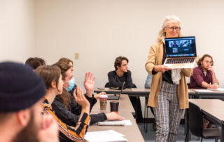 woman walking with computer, students smile and wave at people on the screen